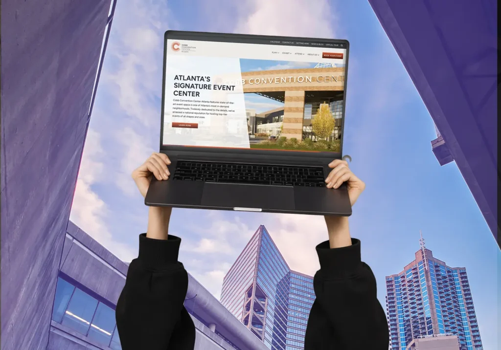 Hands holding a laptop displaying Cobb Convention Center's website with Atlanta skyline in the background